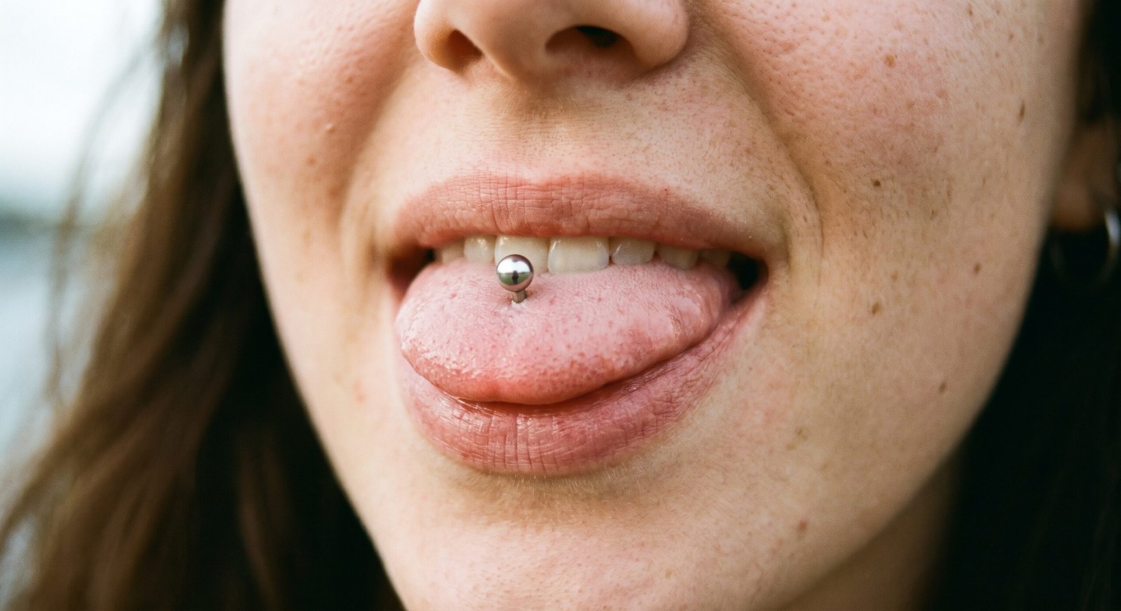 Piercing vertical tradicional na língua, com terminal de esfera visível sobre a língua de fora