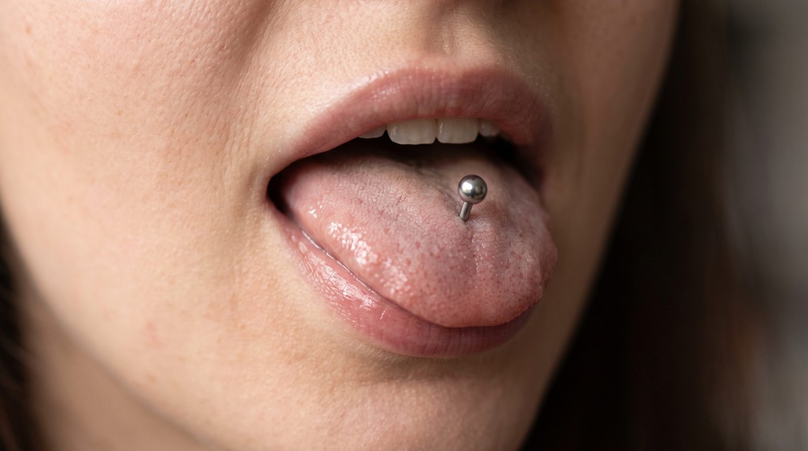 Piercing vertical tradicional na língua, com terminal de esfera, mostrado sobre a língua de fora